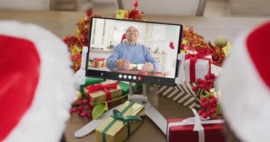 Noel Baba şapkalı çeşitli çiftler, melez bir adamla tablet görüntülü konuşma yapıyorlar. Noel, kutlama, dijital kompozit video.
