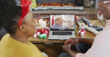 Yılbaşı süsleri olan son sınıf Afro-Amerikan çifti melez bir adamla görüntülü görüşme yapıyor. Noel, gelenek ve kutlama konsepti, dijital kompozit video.