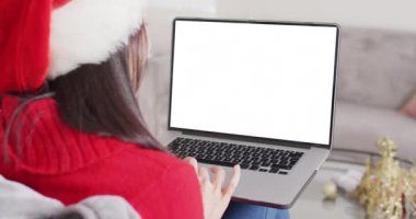 Noel Baba şapkalı beyaz bir kadının Noel 'de boş ekranlı dizüstü bilgisayar kullanması. Noel, şenlik, gelenek ve kutlama konsepti dijital olarak oluşturuldu.