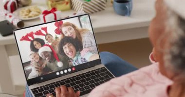 Noel Baba şapkalı kıdemli Afro-Amerikan kadın çeşitli mutlu arkadaşlarıyla dizüstü bilgisayar görüşmesi yapıyor. Noel, şenlik ve iletişim teknolojisi.