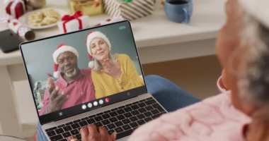 Kıdemli Afro-Amerikan kadın, kıdemli bir çiftle Noel 'de görüntülü görüşme yapıyor. İletişim teknolojisi ve noel, dijital kompozit video.