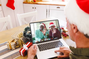 Kıdemli Kafkasyalı adam, kıdemli Afro-Amerikan çiftiyle yılbaşı görüntülü görüşme yapıyor. İletişim teknolojisi ve noel, dijital kompozit görüntü.