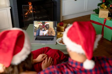 Kafkasyalı çift, Afrika kökenli Amerikalı bir aileyle Noel 'de görüntülü görüşme yapıyor. İletişim teknolojisi ve noel, dijital kompozit görüntü.