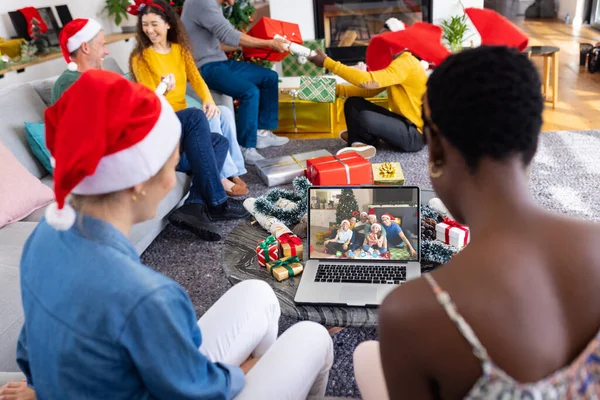 Diverse group of friends having christmas video call with caucasian family. Communication technology and christmas, digital composite image.