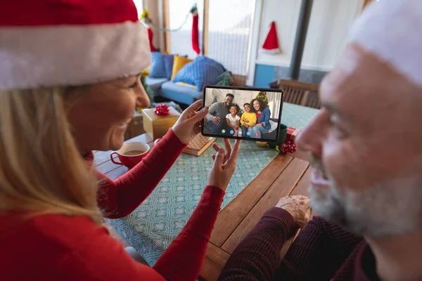 アフリカ系アメリカ人の家族とクリスマスビデオ通話をしているシニア白人夫婦 通信技術とクリスマス デジタル複合画像 — ストック写真