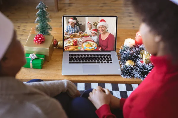African american couple having christmas video call with caucasian family. Communication technology and christmas, digital composite image.
