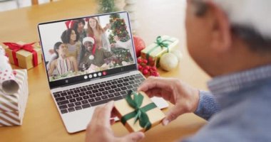 Çift cinsiyetli bir adam, mutlu arkadaşlarıyla dizüstü bilgisayar görüntülü görüşme yapıyor. Noel, şenlik ve iletişim teknolojisi.