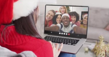 Kafkasyalı, Noel Baba şapkalı bir kadın mutlu arkadaşlarıyla dizüstü bilgisayar görüşmesi yapıyor. Noel, şenlik ve iletişim teknolojisi.