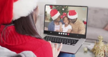 Noel Baba şapkalı beyaz kadın mutlu Afro-Amerikan ailesiyle dizüstü bilgisayar görüşmesi yapıyor. Noel, şenlik ve iletişim teknolojisi.