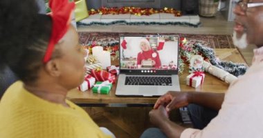 Kıdemli Afro-Amerikan çifti, Kafkasyalı bir kadınla Noel 'de görüntülü görüşme yapıyor. İletişim teknolojisi ve noel, dijital kompozit video.