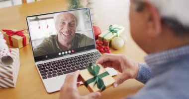 Noel Baba şapkalı melez bir adam beyaz bir adamla laptopla görüntülü görüşme yapıyor. Noel, kutlama, dijital kompozit video.