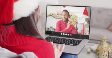 Asyalı kadın, Afrikalı Amerikalı bir adamla Noel 'de görüntülü görüşme yapıyor. İletişim teknolojisi ve noel, dijital kompozit video.