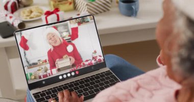 Noel Baba şapkalı Afrikalı Amerikalı bir kadın mutlu beyaz bir kadınla dizüstü bilgisayar görüşmesi yapıyor. Noel, gelenek ve kutlama konsepti, dijital kompozit video.