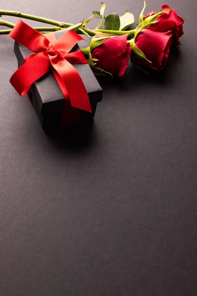 Composition of roses and gift on black background. Valentines day, celebration and copy space, digital composite image.