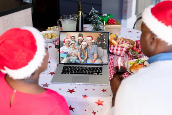 Senior african american couple having christmas video call with caucasian family. Communication technology and christmas, digital composite image.