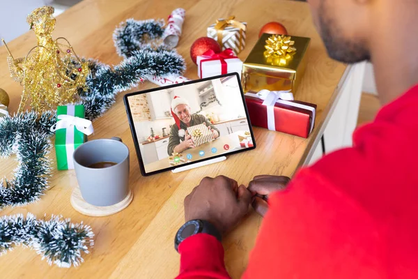 African american man with christmas decorations having video call with happy caucasian man. Christmas, celebration and digital composite image.