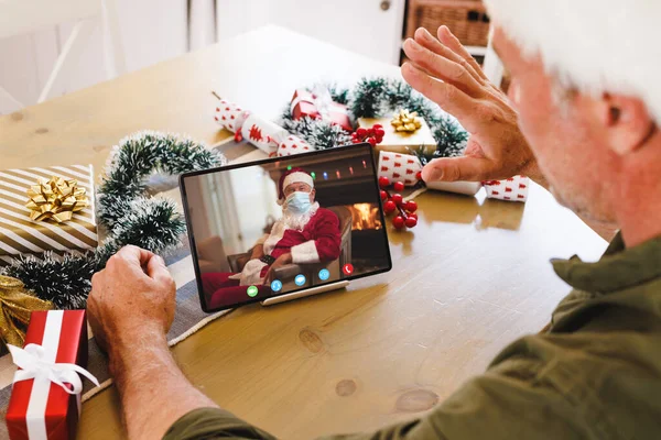 Caucasian man with santa hat having video call with santa claus with face mask. Christmas, celebration and digital composite image.