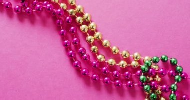Pembe, altın ve yeşil Mardi Gras karnaval boncuklarının pembe arka planda videosu. Karnaval, kostüm, parti malzemeleri, eğlence ve kutlama konsepti..