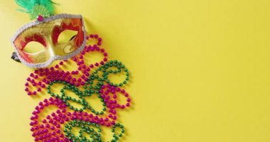 Maskeli balo maskesi, Mardi Gras boncukları ve sarı arkaplandaki tüylerin kopyası. Karnaval, kostüm, parti malzemeleri, eğlence ve kutlama konsepti..