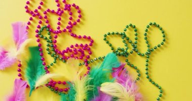 Pembe ve yeşil Mardi Gras karnaval boncukları ve sarı arkaplanda kopyalanmış tüylerin videosu. Karnaval, kostüm, parti malzemeleri, eğlence ve kutlama konsepti..