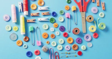 Makas, düğme, raptiye, raptiye, raptiye ve pamuk makaralarının mavi arka planda kalp şeklinde videoları. Dikiş dikme, terzilik, yaratıcılık, el işleri ve hobiler konsepti.