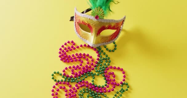 带羽毛的化装舞会面具和带复制空间的黄色背景的玛蒂 格拉丝珠子的视频 狂欢节 盛装打扮 派对道具 欢乐和庆祝的概念 — 图库视频影像