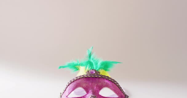コピースペースと白の背景に緑と黄色の羽を持つピンクのマスカレードマスクのビデオ カーニバル ドレスアップ パーティーの小道具 楽しさとお祝いのコンセプト — ストック動画