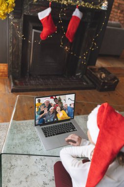 Noel Baba şapkalı beyaz bir kadın mutlu arkadaşlarıyla görüntülü görüşme yapıyor. Noel, kutlama ve dijital kompozit görüntü.