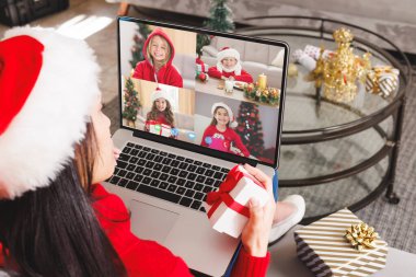 Beyaz kadın, Noel Baba şapkalı mutlu beyaz çocuklarla video görüşmesi yapıyor. Noel, kutlama ve dijital kompozit görüntü.