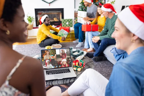 Diverse friends with christmas decorations having video call with happy caucasian friends. Christmas, celebration and digital composite image.