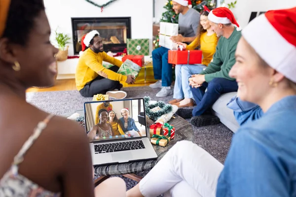 Diverse friends with santa hats having video call with happy diverse friends. Christmas, celebration and digital composite image.