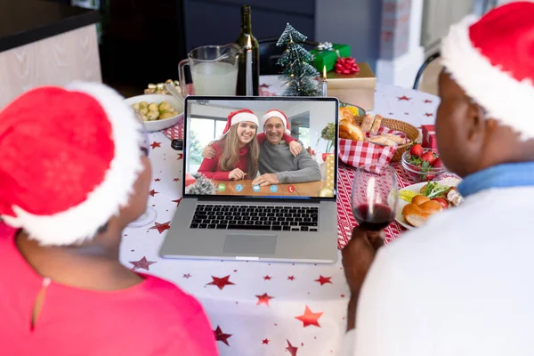 戴着桑塔帽的非洲裔美国人夫妇与快乐的高加索家庭有视频通话 圣诞节 庆祝活动和数码合成图像 — 图库照片