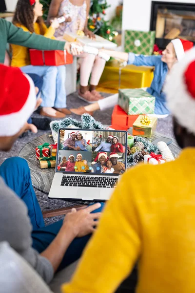Diverse friends with santa hats having video call with happy diverse friends. Christmas, celebration and digital composite image.