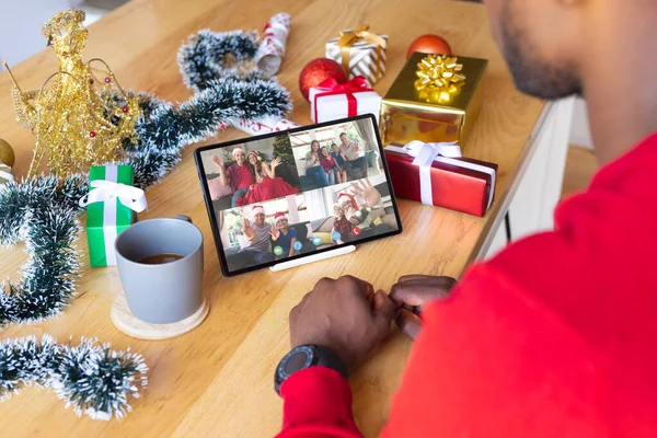 African american man with christmas decorations having video call with happy caucasian friends. Christmas, celebration and digital composite image.