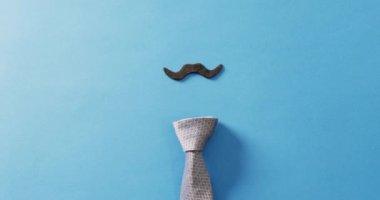 Takma bıyık ve kravatın mavi arka planda fotokopi alanındaki videosu. Babalar günü, kostüm, parti malzemeleri, eğlence ve kutlama konsepti..