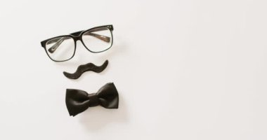 Siyah sahte bıyıklı, gözlüklü ve beyaz arka planda fiyonk kravatlı bir video. Babalar günü, kostüm, parti malzemeleri, eğlence ve kutlama konsepti..