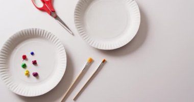 Beyaz zemin üzerinde boya, boya fırçası ve makas ile fotokopi alanı olan kağıt tabakaların videosu. Sanat, resim, yaratıcılık, zanaat ve hobiler kavramı.