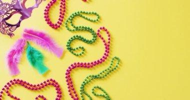 Pembe maske, Mardi Gras karnaval boncukları ve sarı arkaplanda kopyalanmış tüylerin videosu. Karnaval, kostüm, parti malzemeleri, eğlence ve kutlama konsepti..