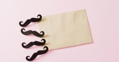 Dört siyah sahte bıyığın ve pembe arka planda fotokopi alanı olan sarı zarfın videosu. Babalar günü, kostüm, parti malzemeleri, eğlence ve kutlama konsepti..