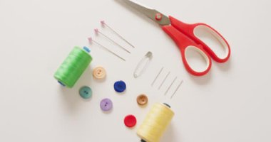 Makas, düğme, raptiye ve pamuk makaralarının beyaz arka planda sıralandığı video. Dikiş dikme, terzilik, yaratıcılık, el işleri ve hobiler konsepti.