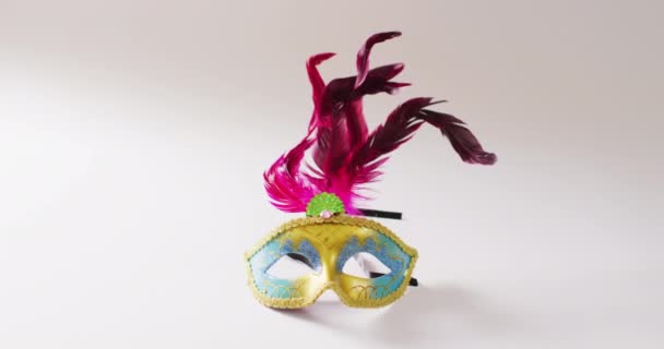 コピースペースと白の背景にピンクの羽を持つ黄色と青のマスカレードマスクのビデオ カーニバル ドレスアップ パーティーの小道具 楽しさとお祝いのコンセプト — ストック動画