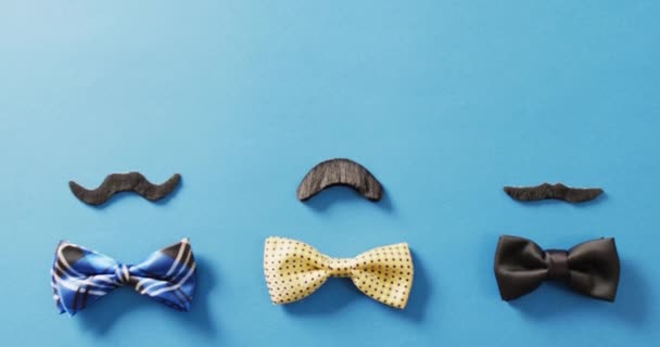 三个不同的假胡子和领结在蓝色背景与复制空间的视频 父亲节 派对道具 欢乐和庆祝的概念 — 图库视频影像