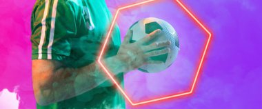 Beyaz tenli erkek oyuncunun, renkli arka planda aydınlanmış altıgenle topu tutmasının orta kısmı. Boşluğu kopyala, kompozit, spor, futbol, rekabet, neon, illüstrasyon, parlama, duman ve soyut.
