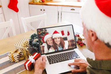 Kafkasyalı kıdemli bir adam Kafkasyalı bir kadın ve kızıyla Noel 'de görüntülü görüşme yapıyor. İletişim teknolojisi ve noel, dijital kompozit görüntü.