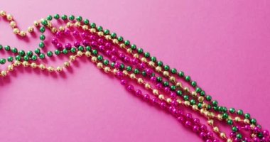 Pembe, altın ve yeşil Mardi Gras karnaval boncuklarının pembe arka planda videosu. Karnaval, kostüm, parti malzemeleri, eğlence ve kutlama konsepti..