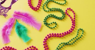 Pembe maske, Mardi Gras karnaval boncukları ve sarı arkaplanda kopyalanmış tüylerin videosu. Karnaval, kostüm, parti malzemeleri, eğlence ve kutlama konsepti..