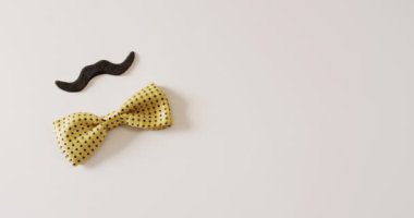 Siyah sahte bıyıklı ve sarı benekli papyonlu beyaz arka planda fotokopi alanı olan bir video. Babalar günü, kostüm, parti malzemeleri, eğlence ve kutlama konsepti..