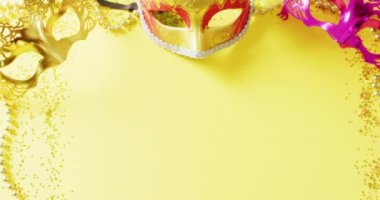 Üç maskeli balo maskesi, Mardi Gras boncukları ve sarı arka planda fotokopi alanı olan konfetilerin videosu. Karnaval, kostüm, parti malzemeleri, eğlence ve kutlama konsepti..
