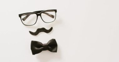 Siyah sahte bıyıklı, gözlüklü ve beyaz arka planda fiyonk kravatlı bir video. Babalar günü, kostüm, parti malzemeleri, eğlence ve kutlama konsepti..