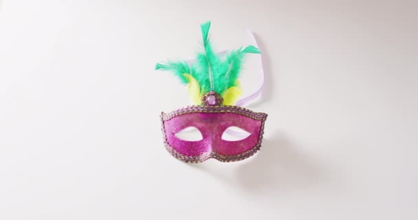 コピースペースと白の背景に緑と黄色の羽を持つピンクのマスカレードマスクのビデオ カーニバル ドレスアップ パーティーの小道具 楽しさとお祝いのコンセプト — ストック動画